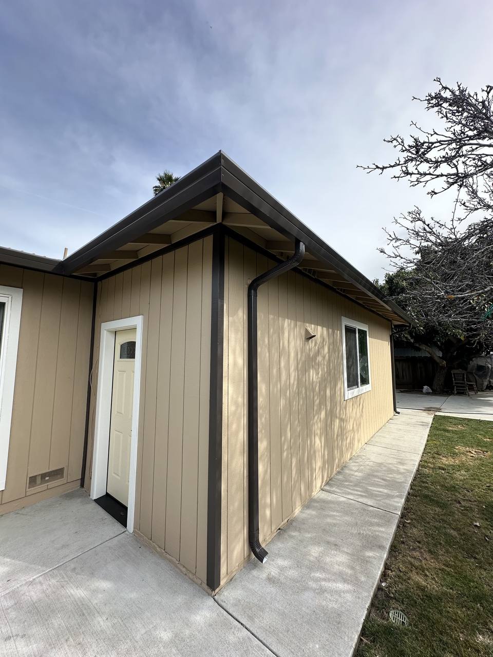 Newly installed seamless gutter and downspout wrapping the roofline of a tan stucco home