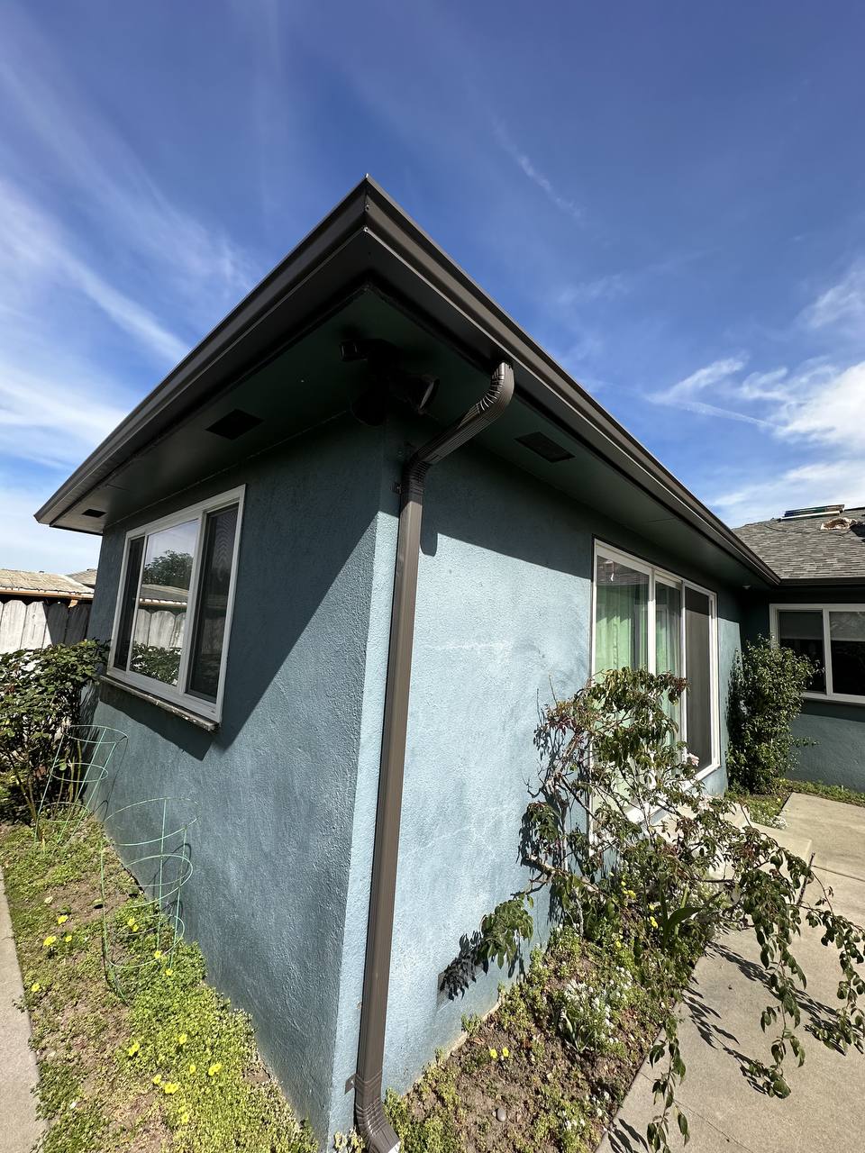 Dark bronze gutter and downspout installed on the corner of a blue stucco home