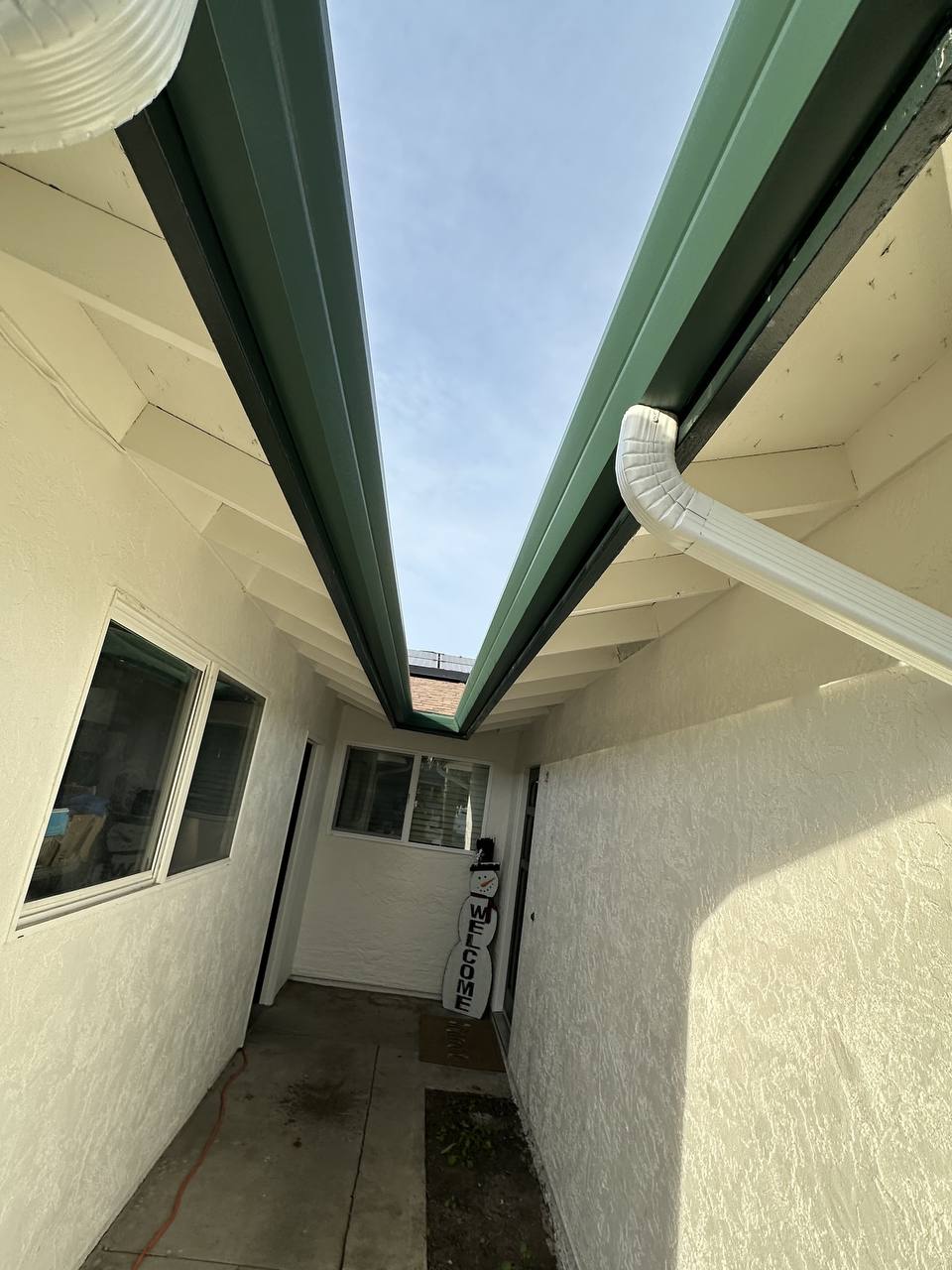 Dual roofline valley with gutters and downspout meeting above a covered walkway