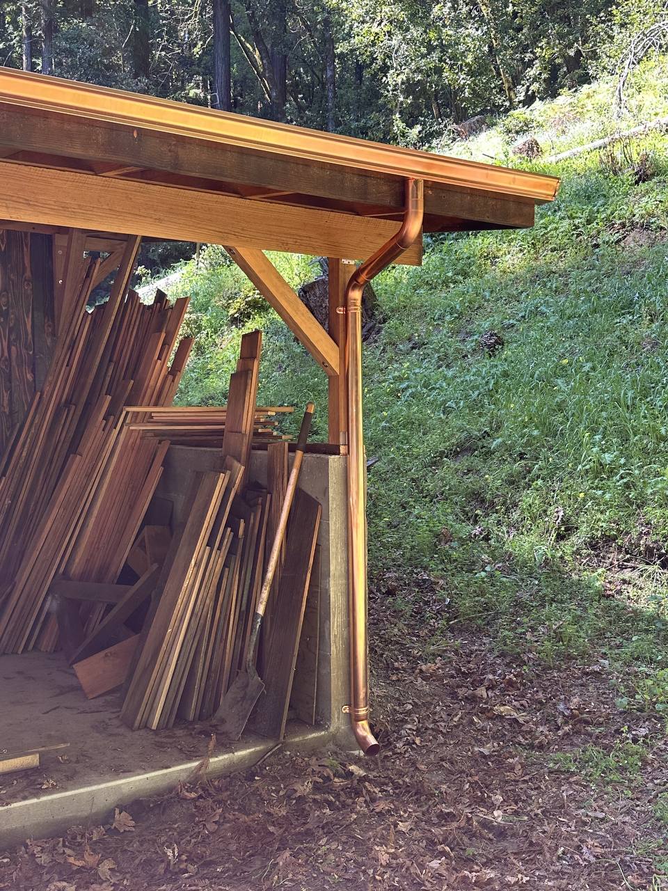 Copper-toned gutter and downspout installed on a wood-framed covered structure