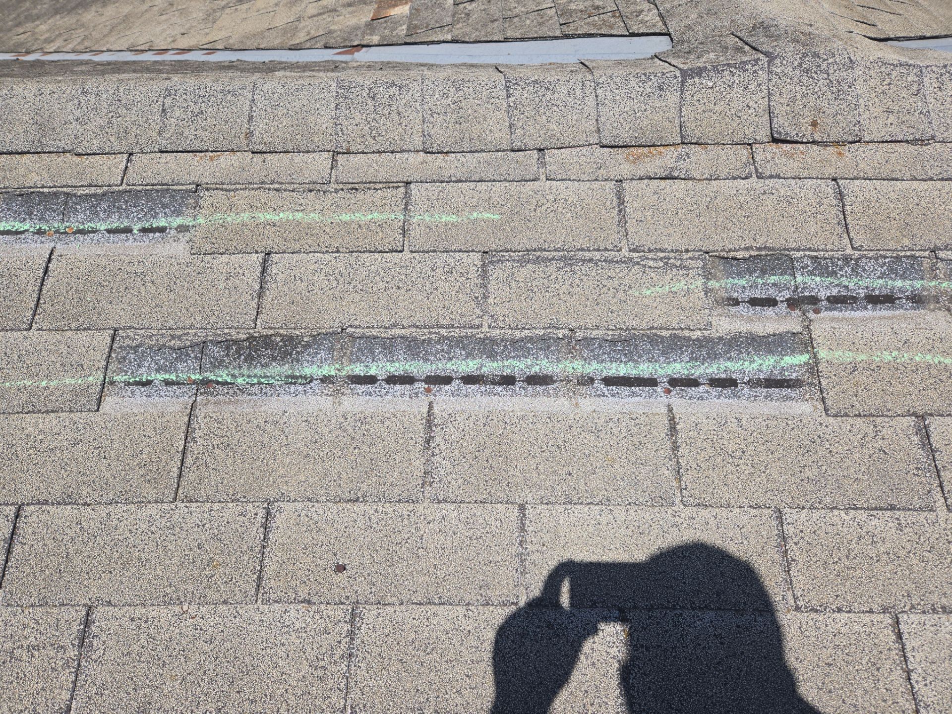 Roof ridge and hip sections chalk-marked for wind damage during an insurance claim assessment