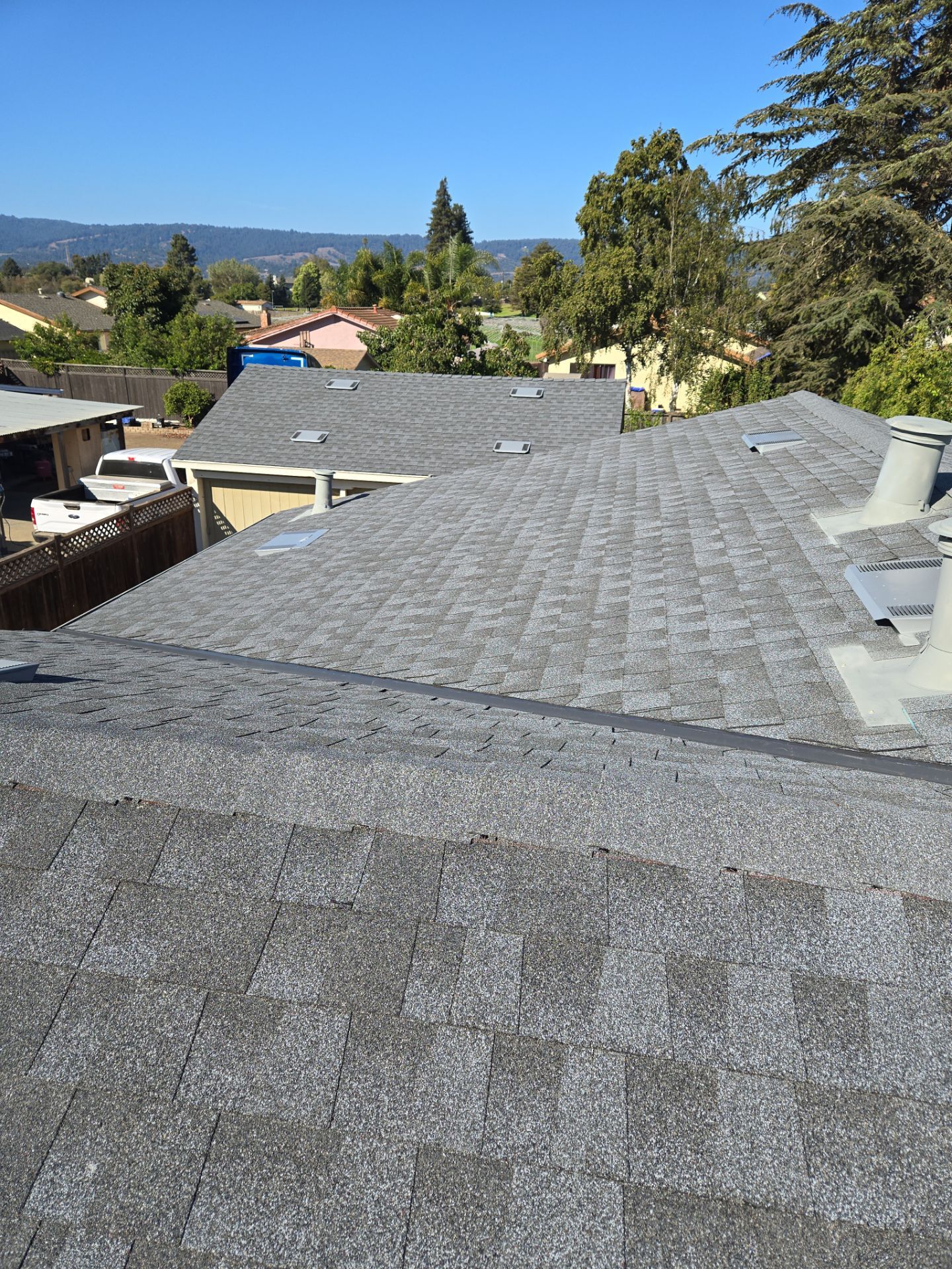 Roof-level view across storm-damaged shingles toward the surrounding neighborhood and hills